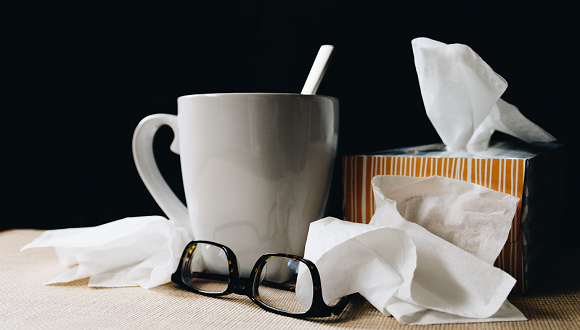white ceramic mug on white table beside black eyeglasses and box of tissues